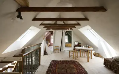 Idee per ristrutturare casa antica: mansarda luminosa con travi a vista, tappeto persiano, teepee e tavolino per bambini.