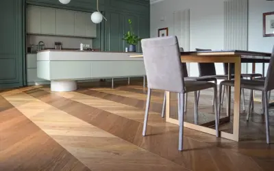 Un elegante parquet a spina di pesce in legno crea un motivo a zig-zag, che si estende dalla cucina moderna alla zona pranzo.