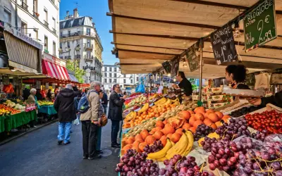 Frukt och grönsaksstånd på en livlig loppmarknad i Paris. Folk handlar bland färska druvor, apelsiner och tomater.