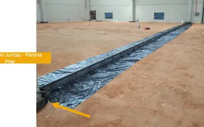 Instalación de una solera de hormigón con armadura metálica sobre plástico negro en interior de nave.