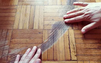 Mani sul parquet rovinato, graffi e segni evidenti. Si cerca una soluzione per pulire e ripristinare il legno.