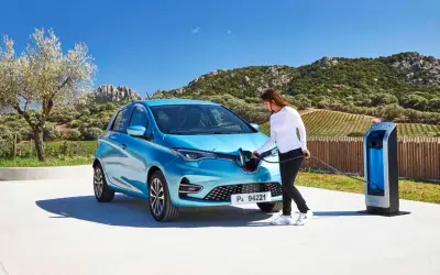 Une femme branche sa Renault Zoé bleue à une borne de recharge. Le temps de recharge zoe 22kw est rapide, parfait pour profiter du paysage.