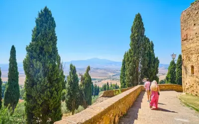 Coppia in cammino durante un tour Toscana 5 giorni, tra cipressi e colline ondulate sotto un cielo azzurro.