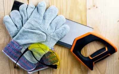 Guantes anticorte niveles, gafas de seguridad y sierra de mano sobre madera.