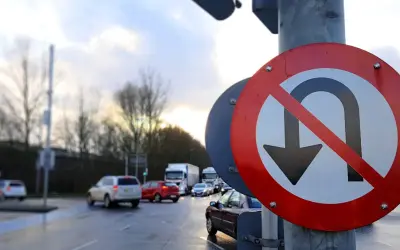 Znak drogowy zakaz zawracania na tle mokrej drogi i samochodów.