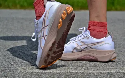 Białe buty do biegania z pomarańczowymi akcentami i charakterystycznym logo. To właśnie asics co to za firma, znana z innowacyjnych rozwiązań dla sportowców.