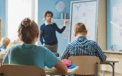 Nauczyciel tłumaczy coś dzieciom w klasie. Zastanawiasz się, ile zarabia nauczyciel klas 1-3?
