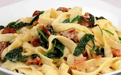 Makaron tagliatelle z kremowym sosem, szpinakiem i kawałkami boczku.