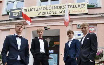 Czterech młodych mężczyzn w garniturach przed budynkiem III Liceum Ogólnokształcącego w Zielonej Górze.