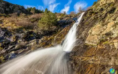 Cascada en un paisaje rocoso y seco, con vegetación escasa. El agua cae con fuerza, creando una estela blanca. Un rincón natural cerca de San Mamés, Madrid.