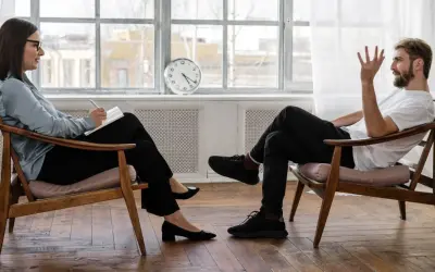 Kobieta i mężczyzna siedzą naprzeciwko siebie, prowadząc rozmowę. Klaryfikacja psychologia w trakcie sesji terapeutycznej.