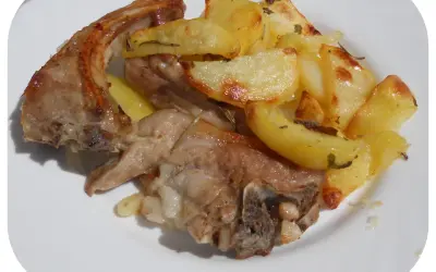 Un succulento agnello gratinato al forno, servito con patate dorate e profumate al rosmarino su un piatto bianco.