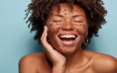 Mujer sonríe con la cara cubierta de exfoliante, mostrando cómo exfoliar la piel para un brillo radiante.