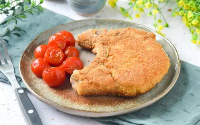 Cotoletta alla milanese dorada y crujiente, acompañada de tomates cherry asados. Un plato clásico y delicioso.