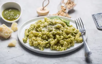 Pyszny makaron z pesto, posypany parmezanem, z dodatkiem świeżej bazylii i orzeszków piniowych.