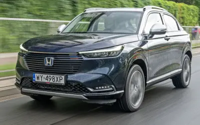 Ciemnogranatowy Honda HR-V na mokrej drodze. Nowoczesne reflektory i grill podkreślają jego dynamiczny charakter. Silniki tej generacji zapewniają oszczędność i płynność jazdy.