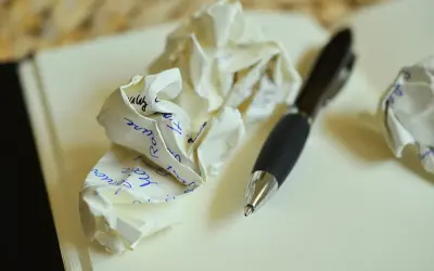 Zgniecione kartki z tekstem, być może próby napisania zaproszenia na ślub. Długopis obok sugeruje proces twórczy.