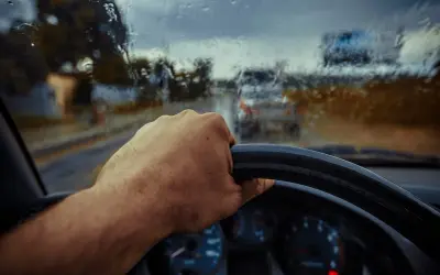 Deszczowa pogoda, ręka na kierownicy, a auto nie odpala. Widać deszcz na szybie i inne samochody w oddali.