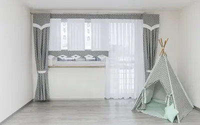 Szare zasłony w gwiazdki i białe firanki idealnie pasują na okno do pokoju młodzieżowego. Obok namiot tipi.