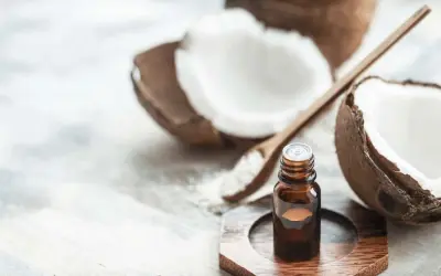 A small bottle of coconut oil sits near a halved coconut and a wooden spoon with coconut flakes. This image prompts the question: is coconut oil safe for cats?
