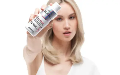 Frau zeigt L'Oréal Elvital Bond Repair Pre-Shampoo gegen extrem trockene Haare. Vorher-Nachher-Effekt für geschädigtes Haar.