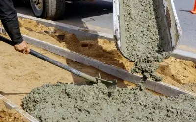 Robotnik rozprowadza łopatą świeży cement z wodą bez piasku, wylewany z betoniarki na budowie.
