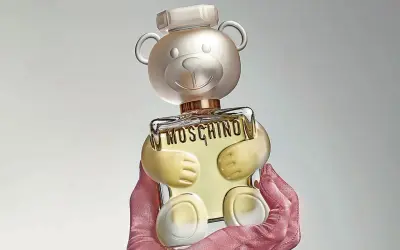 Różowe rękawiczki trzymają uroczy flakon perfum Moschino Toy 2 w kształcie misia.