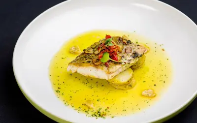 Filet ryby na plastrach ziemniaków, polany bogatym, złocistym sosem maślano cytrynowym, ozdobiony ziołami i suszonymi pomidorami.