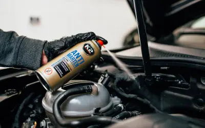 Ręka w rękawiczce rozpyla środek "Anti Marten" w komorze silnika, chroniąc auto przed kunami.