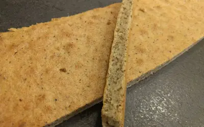 Un biscuit joconde noisette, fin et doré, est coupé en deux. Une fine tranche repose sur une plus grande pièce.