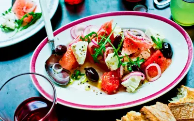 En uppfriskande melon och fetaostsallad med oliver, rödlök och ruccola, serverad på en tallrik med en sked.