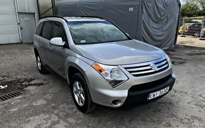 Srebrny Suzuki XL7 zaparkowany przed szarym namiotem.