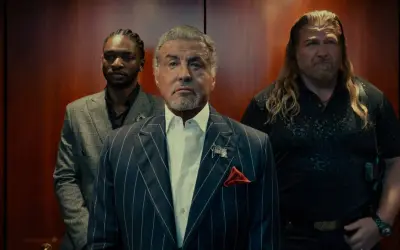 Sylvester Stallone i en serie, flankerad av två män i en hiss.