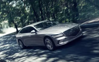 Silver Genesis G80 Sverige glider genom en skogsväg, skuggor dansar över bilen.
