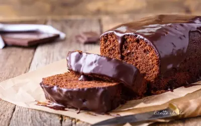 Plumcake al cioccolato con glassa lucida e due fette tagliate, su carta da forno e legno.