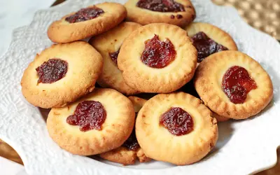 Stos ciastek bez jajek z dżemem w środku, ułożonych na białej paterze. Idealne na podwieczorek.