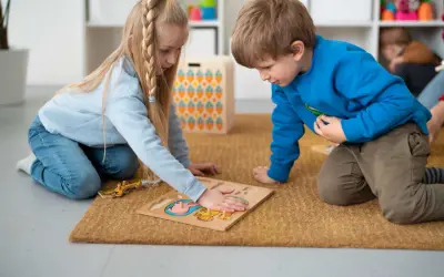 Dzieci na dywanie układają puzzle, ćwicząc spostrzegawczość. To nauka przez zabawę, zgodna z metodą Montessori.
