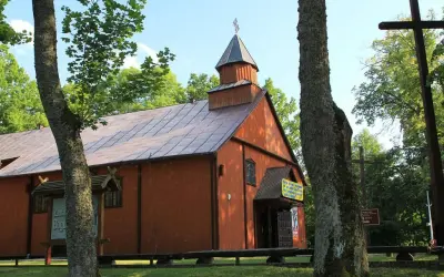 Drewniana cerkiew w Studzienicznej, jedna z lokalnych atrakcji, otoczona zielenią. Obok krzyż.