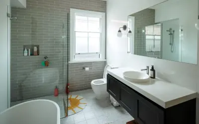 Baño moderno con ducha sin mampara, bañera exenta, lavabo sobre encimera y WC. Azulejos grises y suelo estampado.