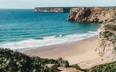 Ein einsamer Surfer genießt die Wellen am Sagres Strand, umgeben von steilen Klippen und dem weiten Atlantik.