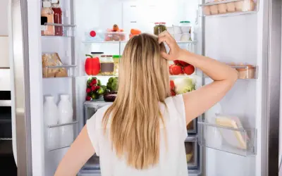 Donna confusa davanti al frigo pieno di cibo, con il desiderio di mangiare e non ingrassare, ma lo stress la blocca.