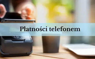 Zbliżenie na terminal płatniczy i kubek kawy. Dłoń trzyma smartfon, gotowa do płatności telefonem.