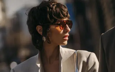 Frau mit einem frechen Pixie Cut, Sonnenbrille und Blazer.