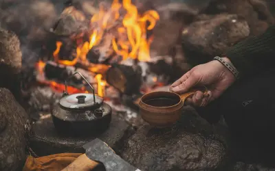 Vid en sprakande eld, med en kaffepanna och en träkopp, kan man brygga kokkaffe. En yxa och handskar ligger bredvid.
