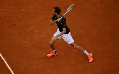 Tenisista wykonuje potężny **backhand** na ceglanej nawierzchni.