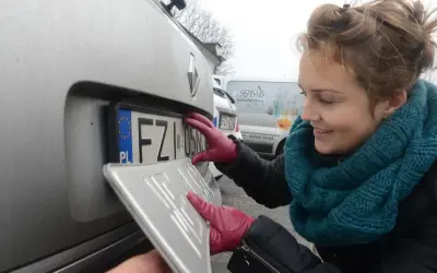 Kobieta w czerwonych rękawiczkach montuje tablicę rejestracyjną. To ważny etap rejestracji wsc.