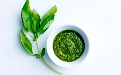Färskt basilika bredvid en skål med hemlagad pesto. Ett perfekt pesto recept för sommaren.