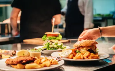 Pyszne jedzenie w restauracji: burgery, frytki, sałatka i kotlet. W tle kucharze przygotowują kolejne dania.