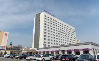 Hotel Mercure Gdynia z parkingiem pełnym samochodów. Elegancki budynek hotelu góruje nad parkingiem.