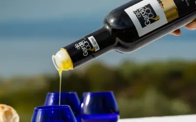 Versando olio Garda DOP in bicchierini blu, con pane fresco sullo sfondo.